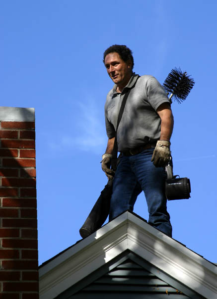 Chimney sweep on a pitched roof feeding rods and a brush down a brick stack