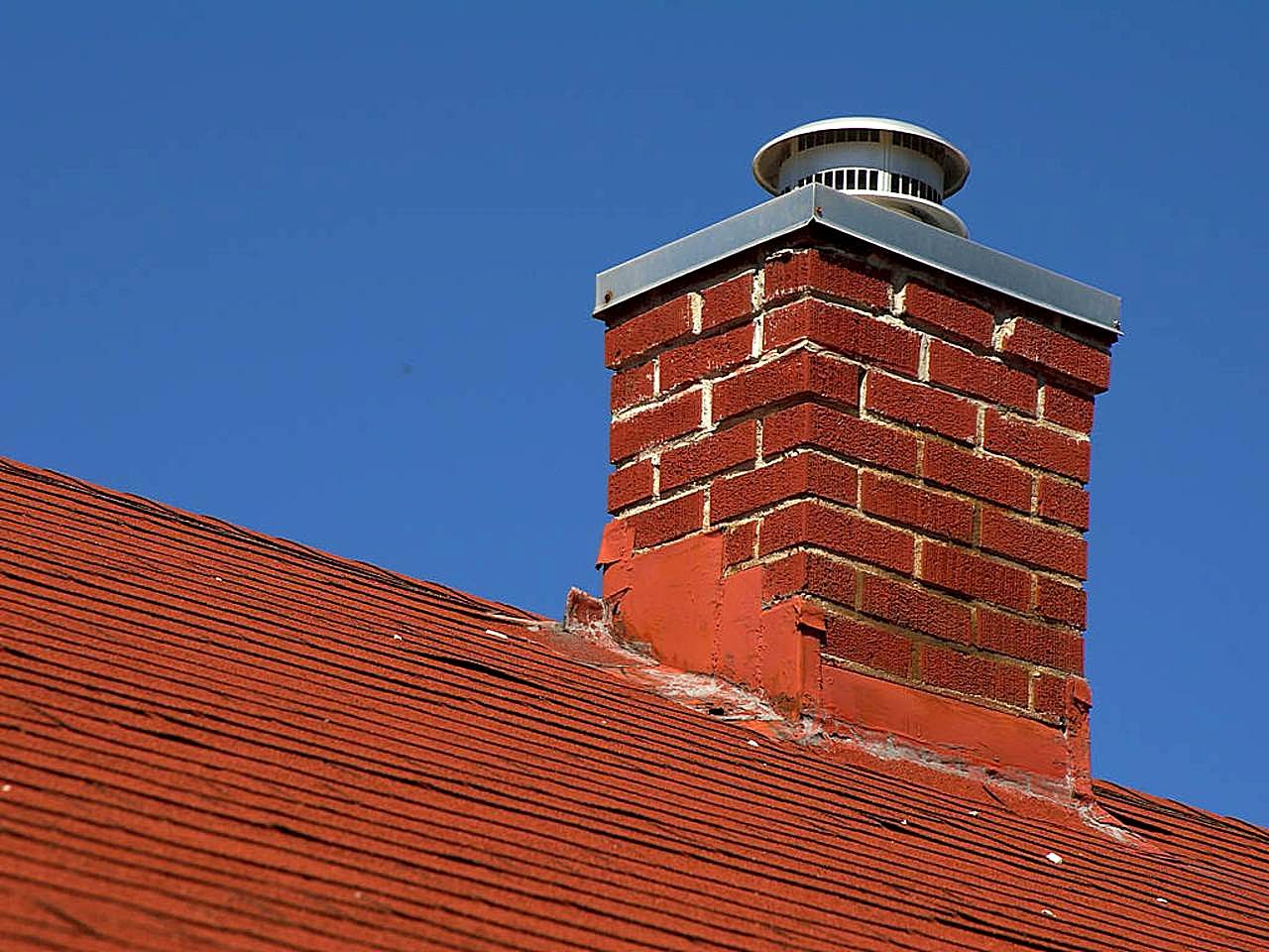 Red brick chimney stack with a concrete crown against a clear sky